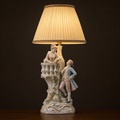 Lit porcelain figurine table lamp with a woman leaning over a balustraded balcony and a man below