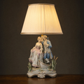 Lit porcelain figurine table lamp with a courting couple beside a small boat and bulrushes