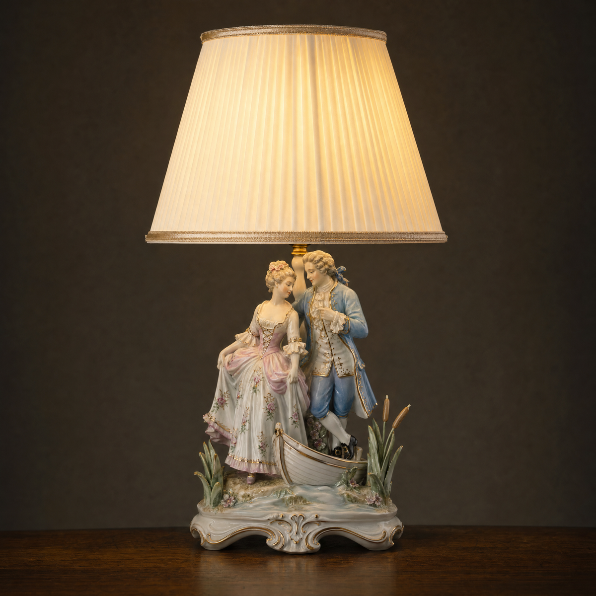 Lit porcelain figurine table lamp with a courting couple beside a small boat and bulrushes