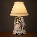 Lit porcelain figurine table lamp with a woman on a flower-trimmed swing and a suitor beside her