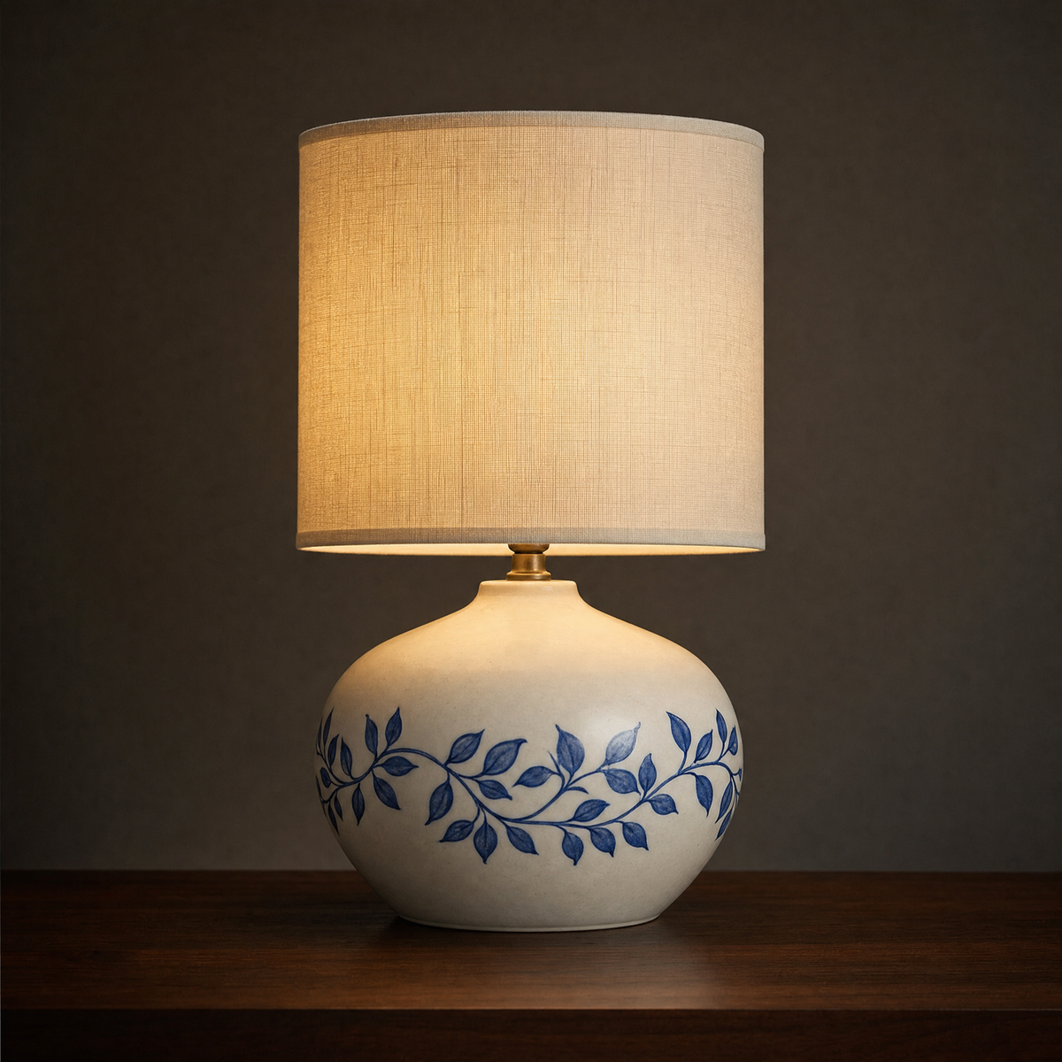 Lit ceramic table lamp with a squat rounded base banded with a trailing cobalt vine and leaves